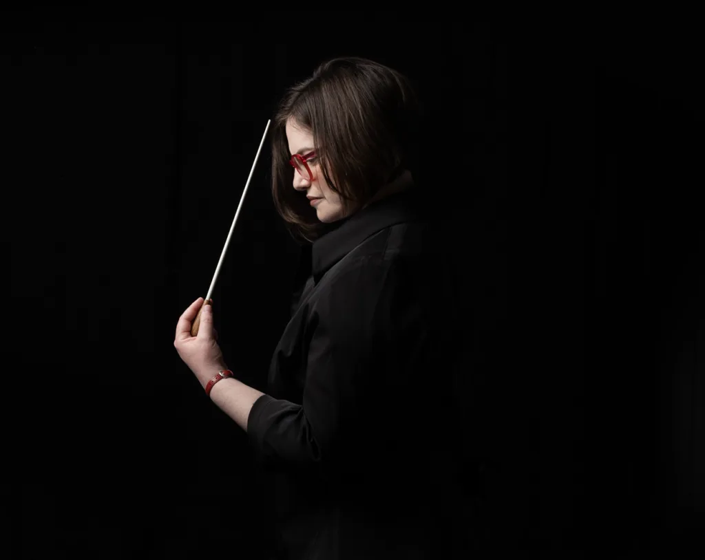 Noam Aviel, music director of Symphony in C, in profile against a black background with a conductor baton raised. Photo: Orr Nir